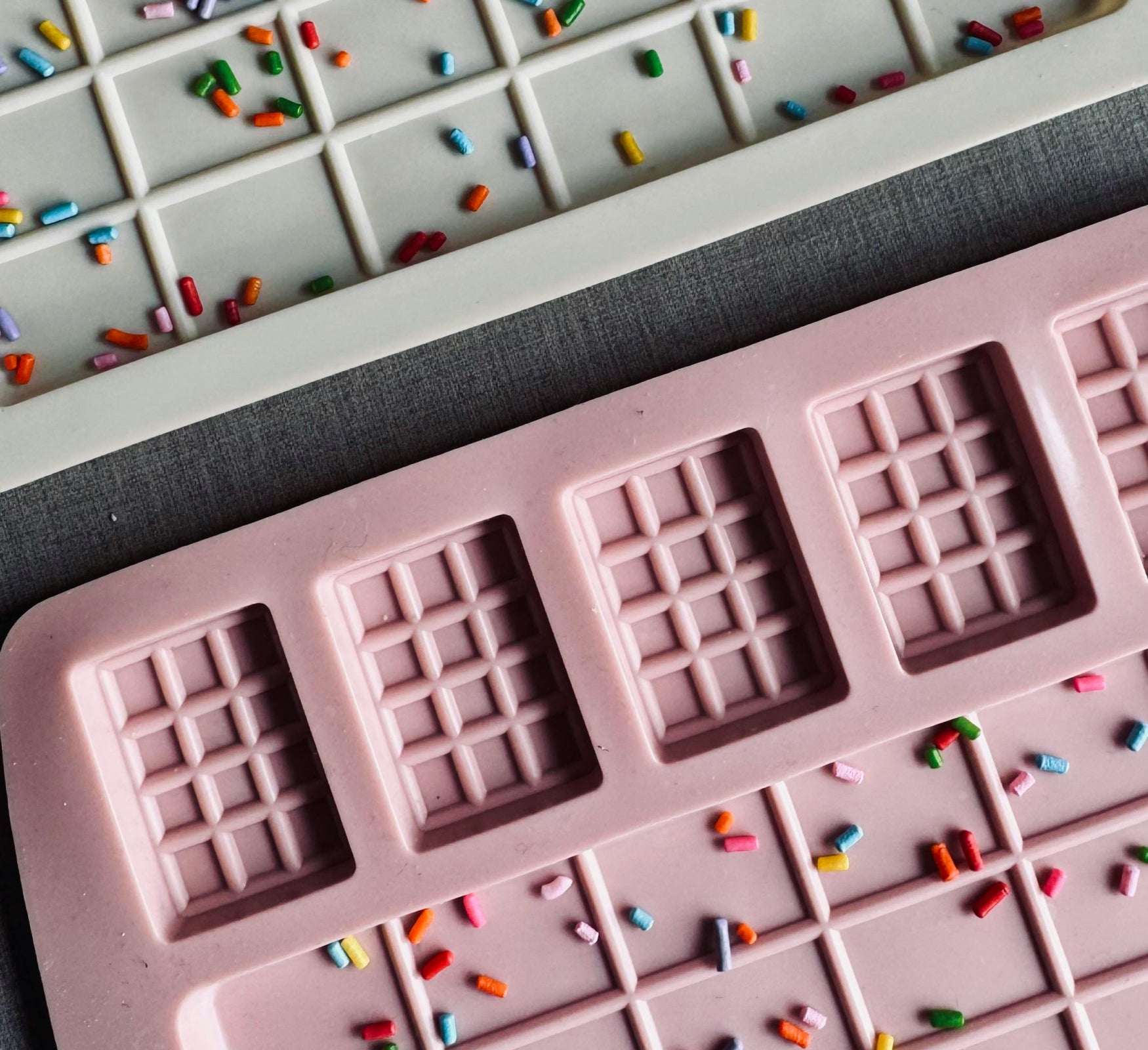 Pink and blue chocolate molds (Moulds) displayed on a dark background, adorned with colorful sprinkles.