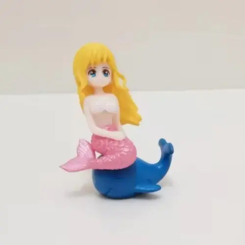 Miniature mermaid figurine with long blonde hair, pink glittery tail, and white shell top sitting on a blue dolphin – perfect for mermaid birthday cake toppers, under the sea themed party décor, and resin ocean figurine collections.