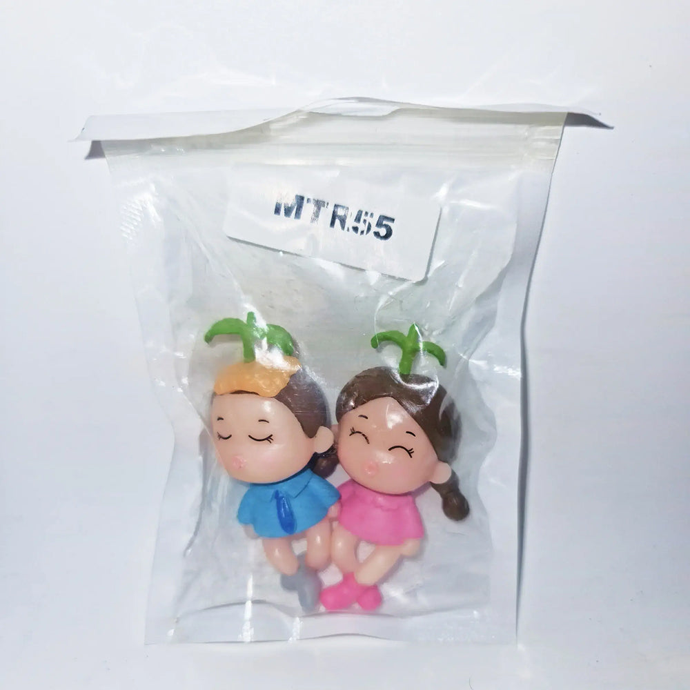 Miniature couple figurines labeled MTRC55 – girl in pink dress and boy in blue with plant sprouts on head, sealed in clear packaging for cute love-themed cake toppers or gifts.