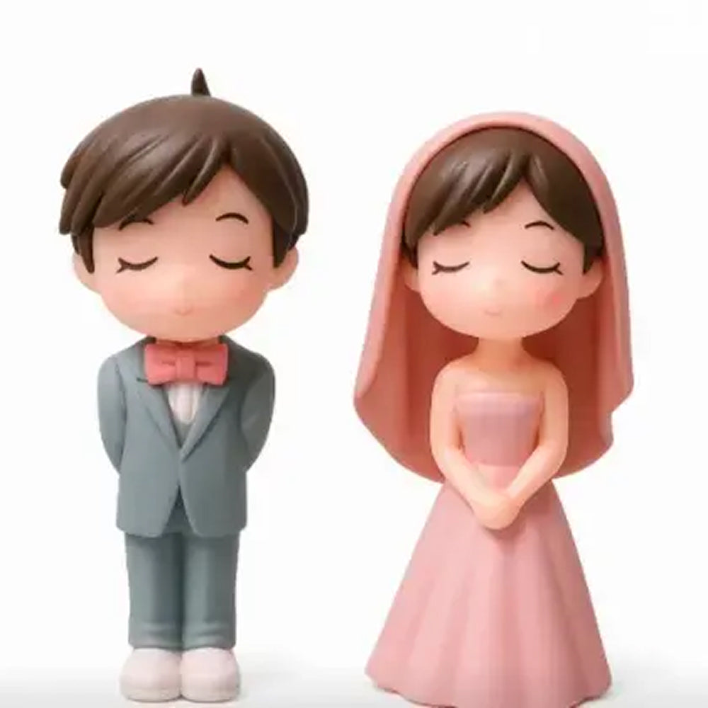 Close-up of wedding-themed couple miniature toys – boy in teal suit with hands behind back and girl in flowing pink dress and veil, both eyes closed in sweet expression, perfect for cakes
