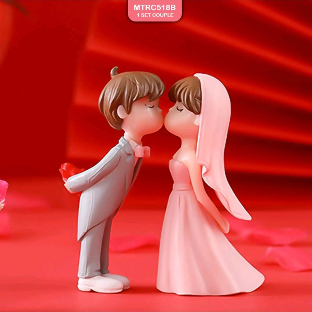 Miniature kissing couple figurine with groom in grey suit and pink bowtie holding red heart behind his back, and bride in pink gown and veil on red backdrop – wedding cake topper decor