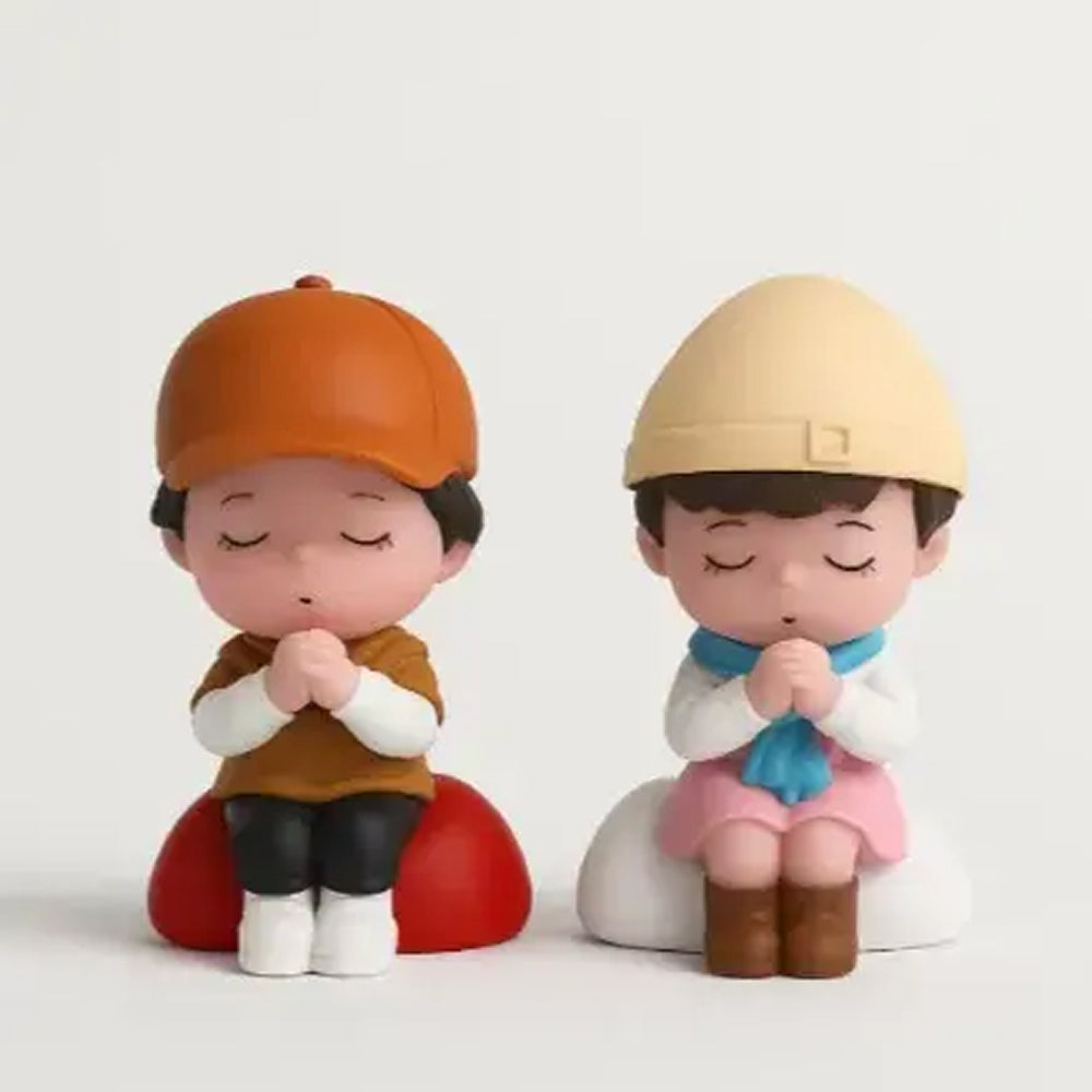 Miniature boy and girl figurines sitting in prayer pose with folded hands, dressed in winter outfits and hats – perfect for cake decoration or gifting