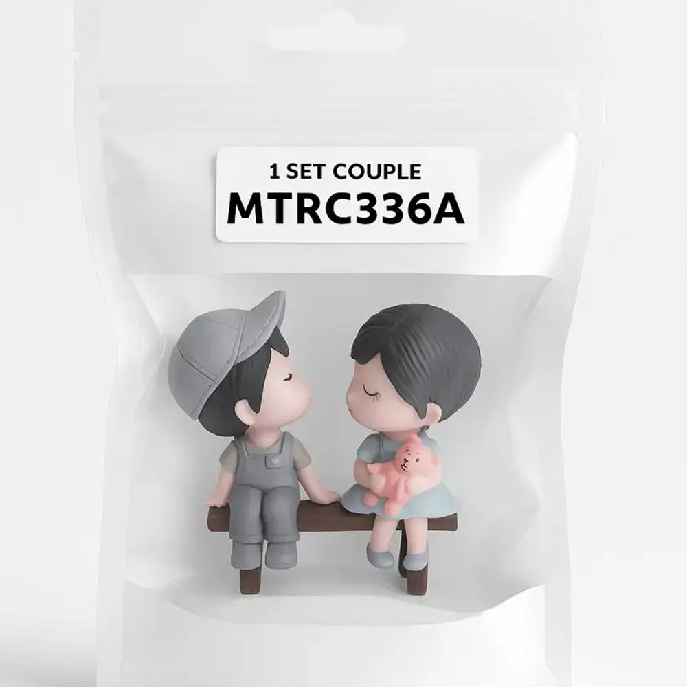 Seated couple miniature toy topper holding a teddy bear, packaged in a transparent pouch labeled MTRC336A – ideal for romantic cake toppers and decoration