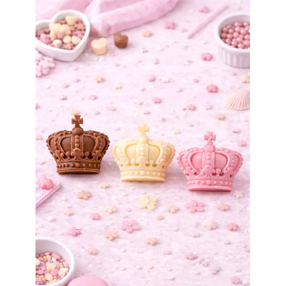 Three crown-shaped candies in brown, yellow, and pink on a pink background with small candies.