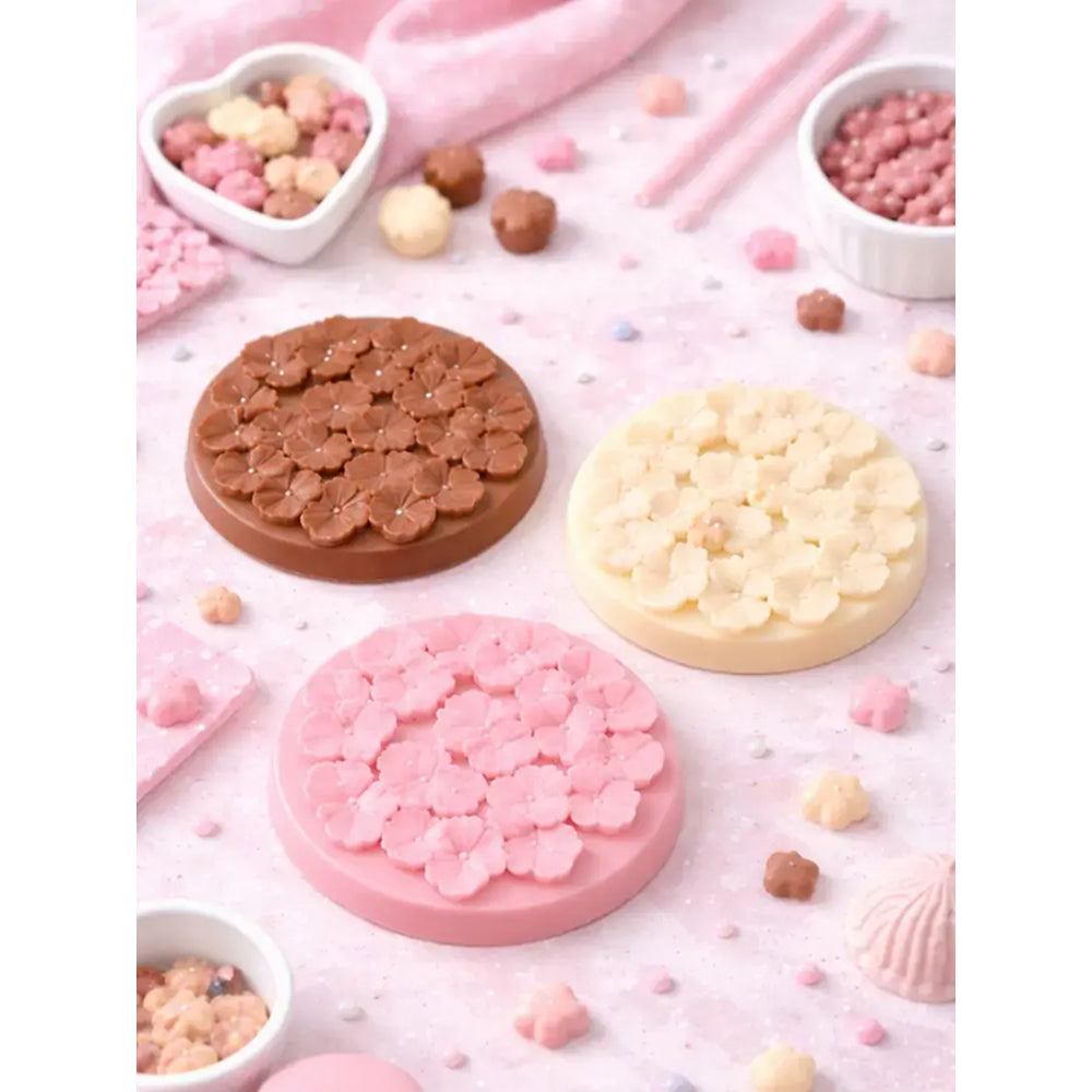 Three round silicone molds with floral patterns on a pink surface with small containers of beads.