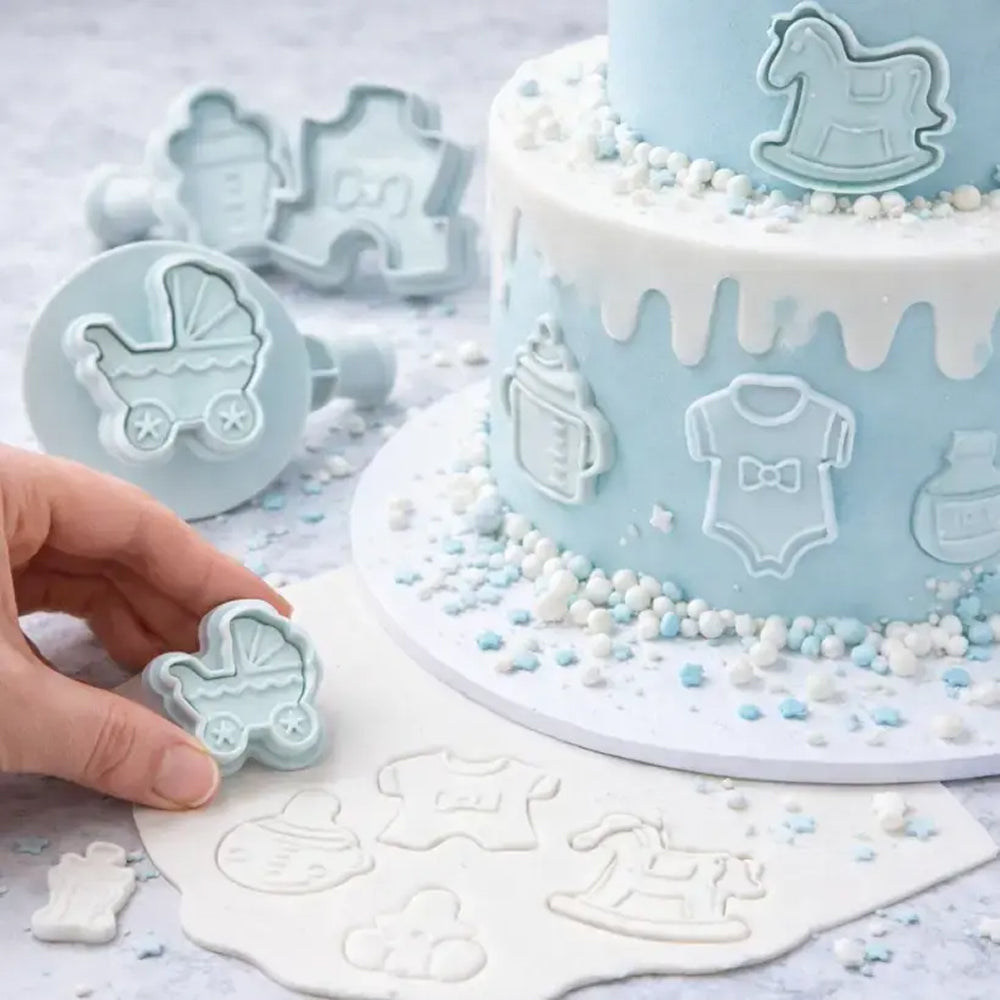 Baby-themed cookie cutters and cake with baby shower decorations on a light gray background