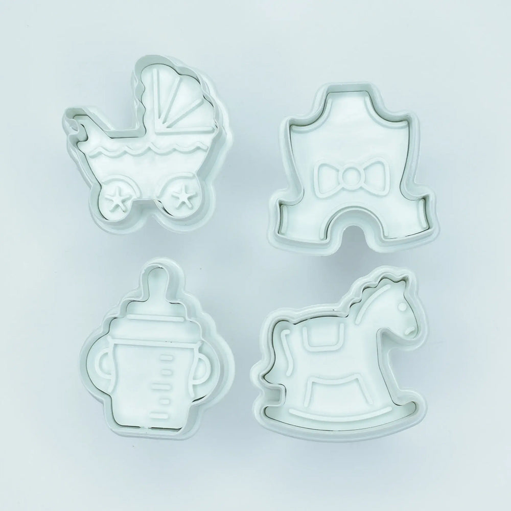 Set of four cookie cutters shaped like a baby carriage, rocking horse, bottle, and hat on a light gray background.