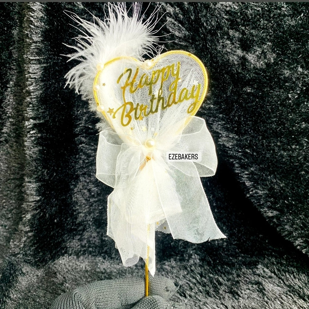 Decorative birthday cake topper with 'Happy Birthday' text and white feathers on a dark background.