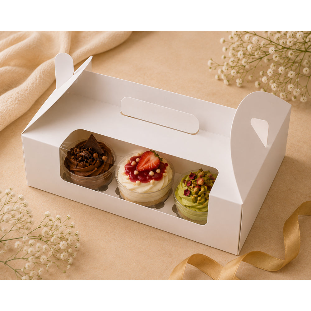 White box with three decorated cupcakes on a beige surface with flowers.