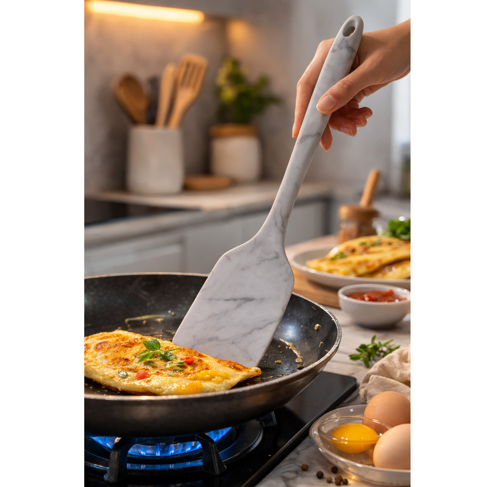 Person using a marble-patterned spatula to flip an omelette in a pan on a stove.