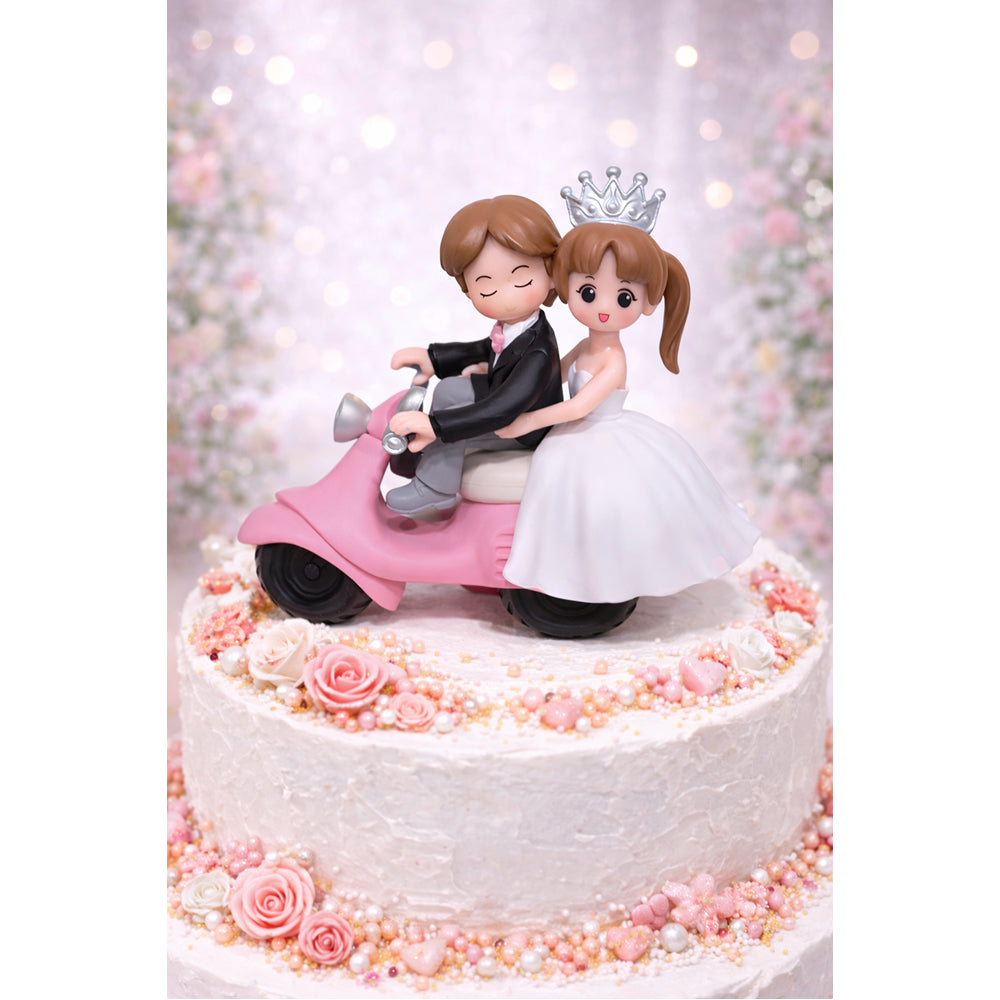 Wedding Miniatures cake topper with couple on a pink scooter against a blurred floral background