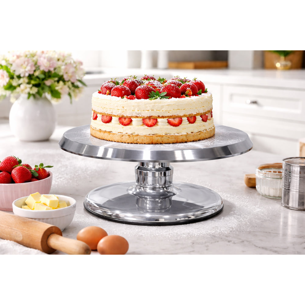 Decorative cake on a turntable with strawberries and kitchen items in the background