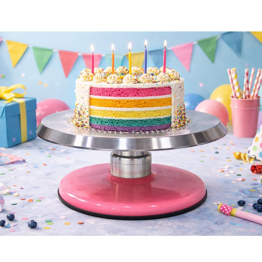 Colorful birthday cake with lit candles on a pink cake stand against a festive background.