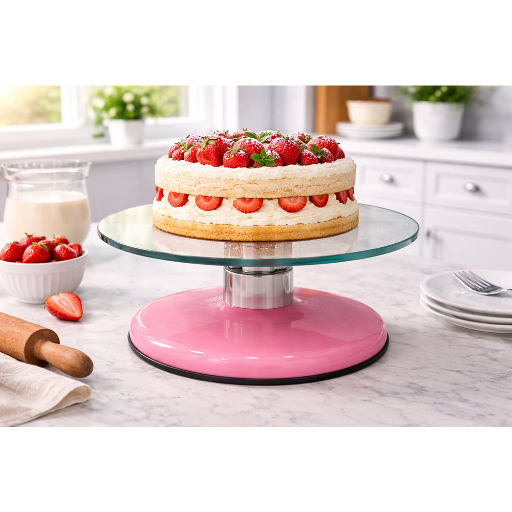 Pink cake stand with a layered cake topped with strawberries on a kitchen counter.