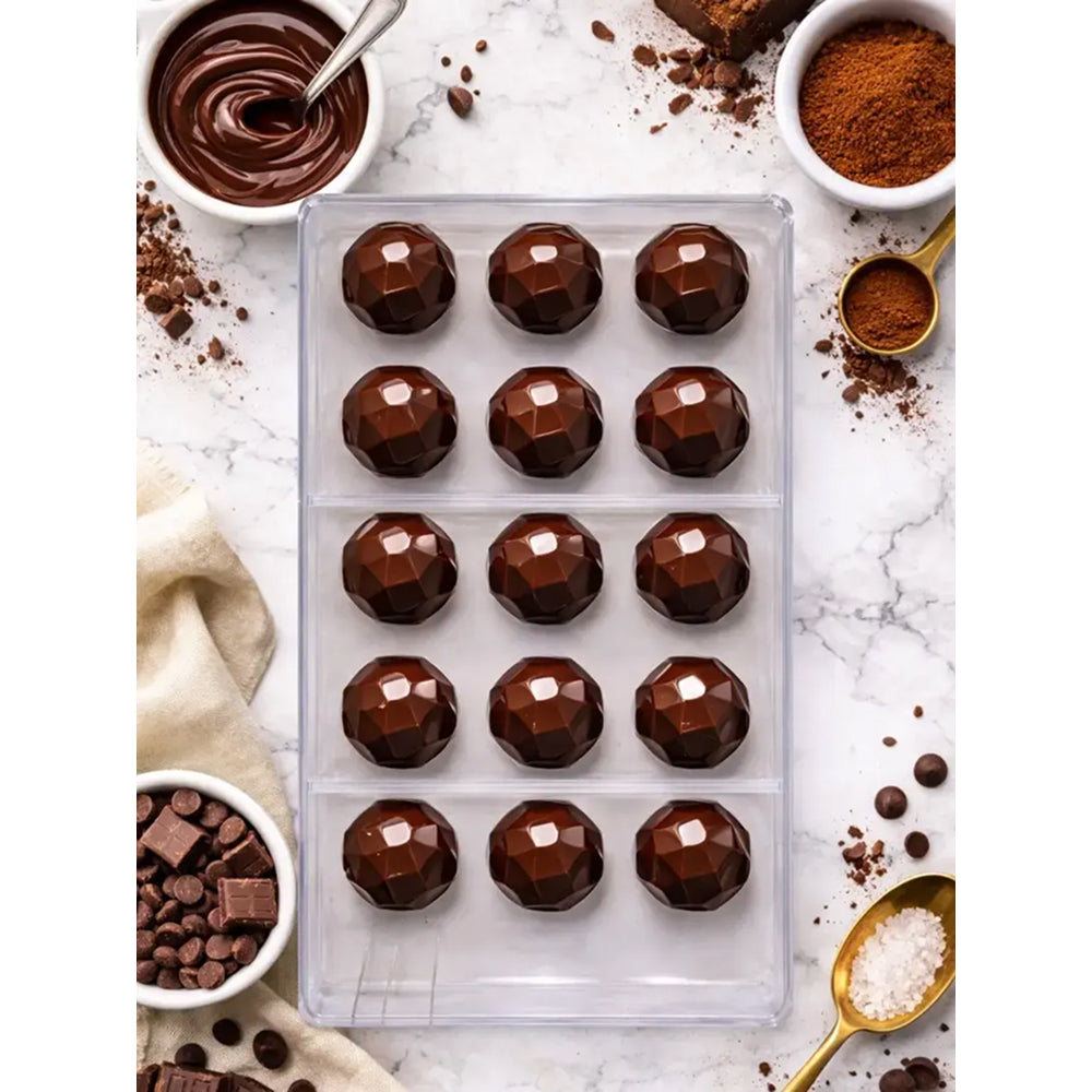 Polycarbonate Chocolate mold with cocoa powder, chocolate chips, and a spoon on a marble surface.