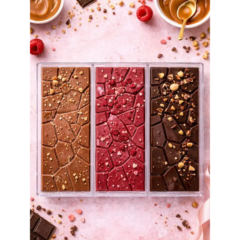 Three different types of polycarbonate chocolate bars in a clear plastic packaging on a pink surface with small bowls and raspberries.