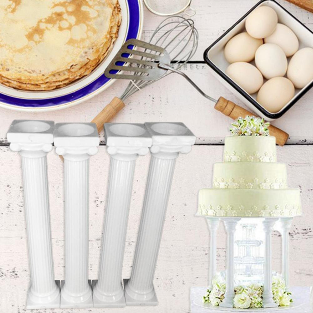 Four white fluted pedestal columns shown with a small wedding cake displayed on one column, alongside baking utensils and eggs on a rustic white surface.