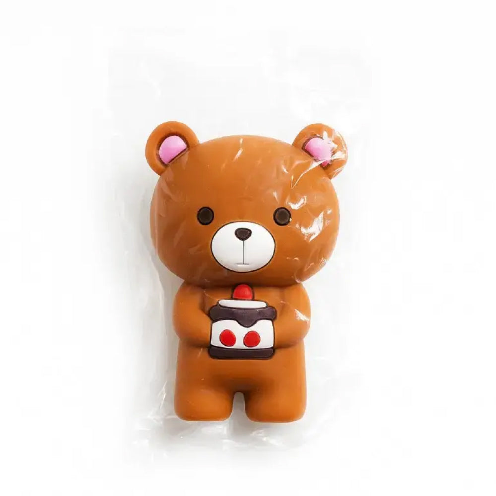 Cute brown teddy bear cake topper miniature sealed in a glossy clear plastic pouch, featuring soft pink inner ears, round dark eyes, and a sweet expression while holding a square dessert with white frosting, red cherry topping, and double red polka dots – perfect for birthday cakes, kawaii themes, and kids' celebrations