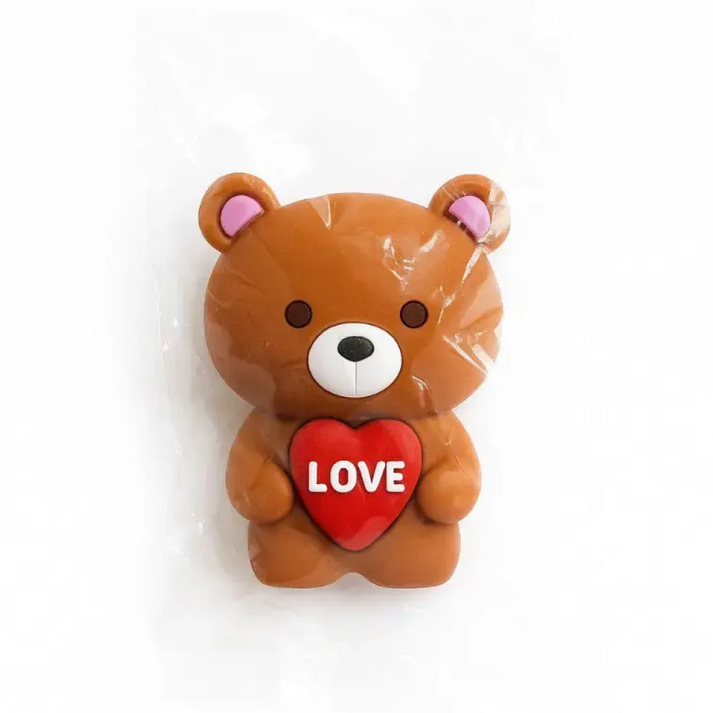 Cute brown teddy bear cake topper sealed in a clear plastic pouch, standing upright with rounded ears, soft pink ear detail, and a bright red heart held close to its chest with the word "LOVE" embossed in bold white letters – ideal for romantic cake decor, gifting themes, anniversaries, and Valentine's Day desserts