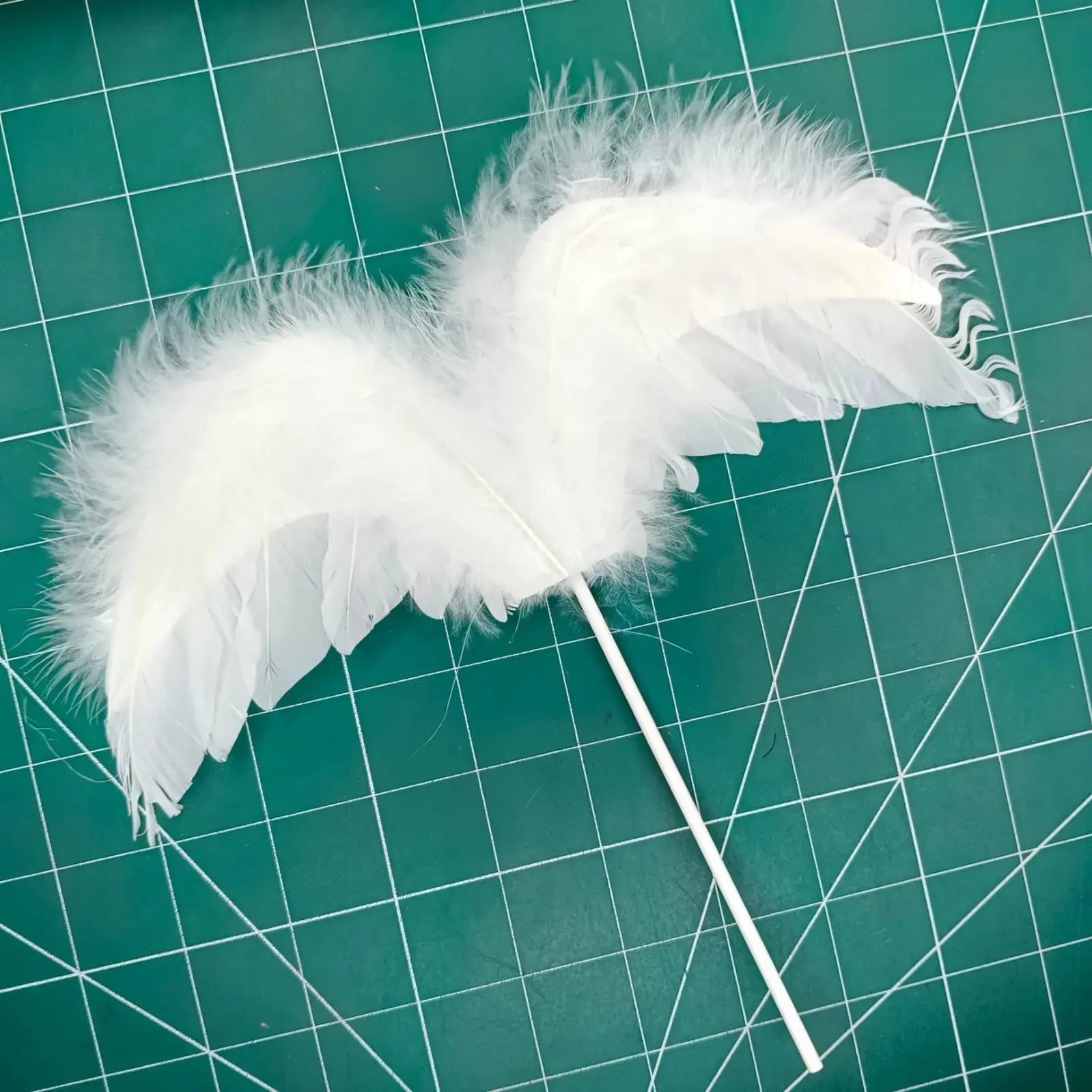White feather wings topper on a green cutting mat with grid lines