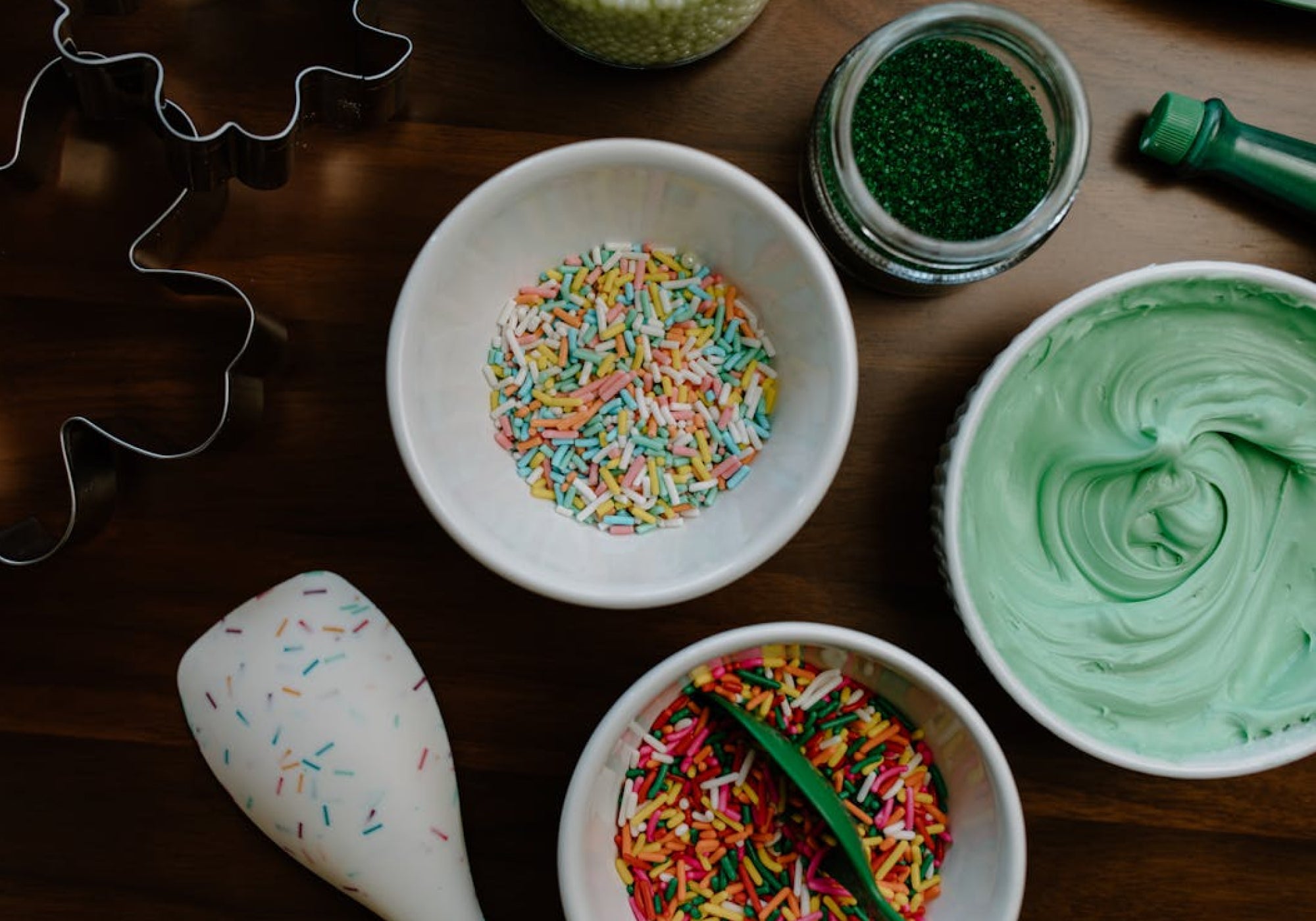 Flat lay of colorful cake sprinkles, green frosting, and decorating tools arranged on wooden surface – perfect for showcasing baking supplies and festive preparation scenes.