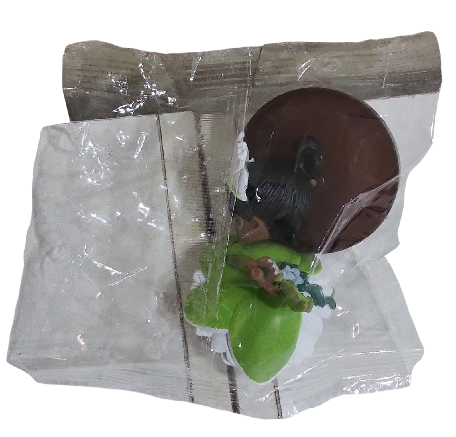 Small figurine of a person in a green outfit with lying with transparent plastic wrap.