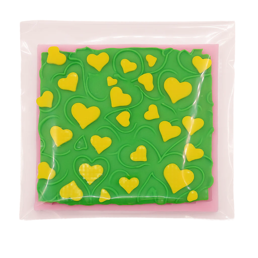 Green and pink textured square silicone fondant mold with yellow heart shapes on a clear background