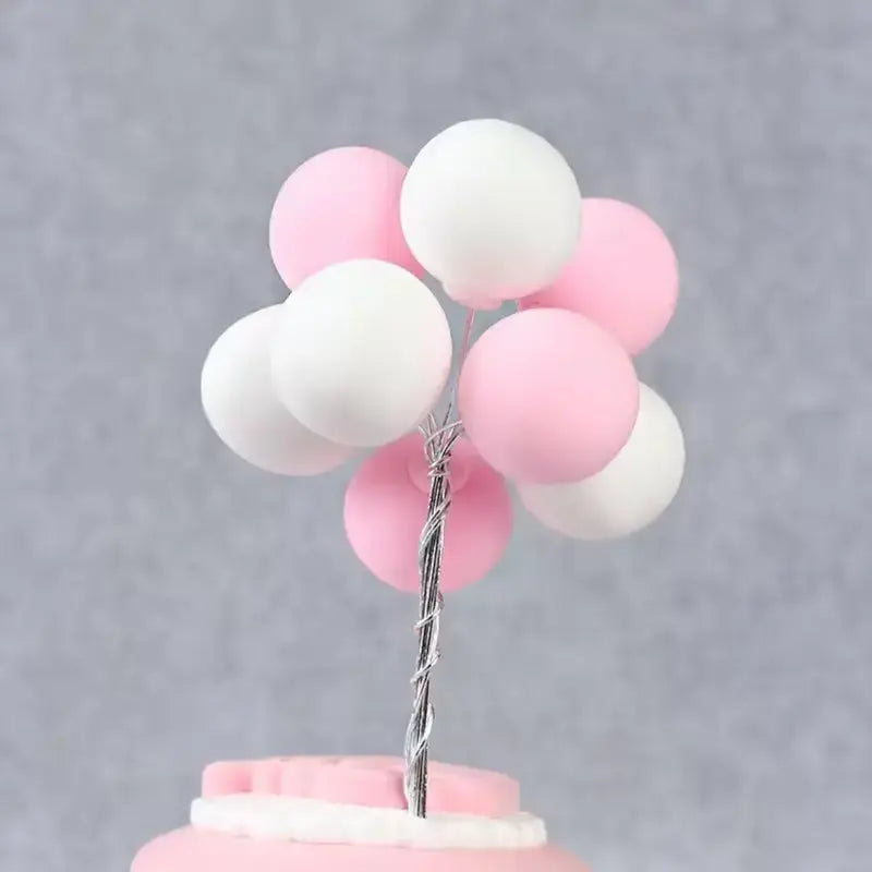 Pink and white balloon cake topper on a cake on a gray background